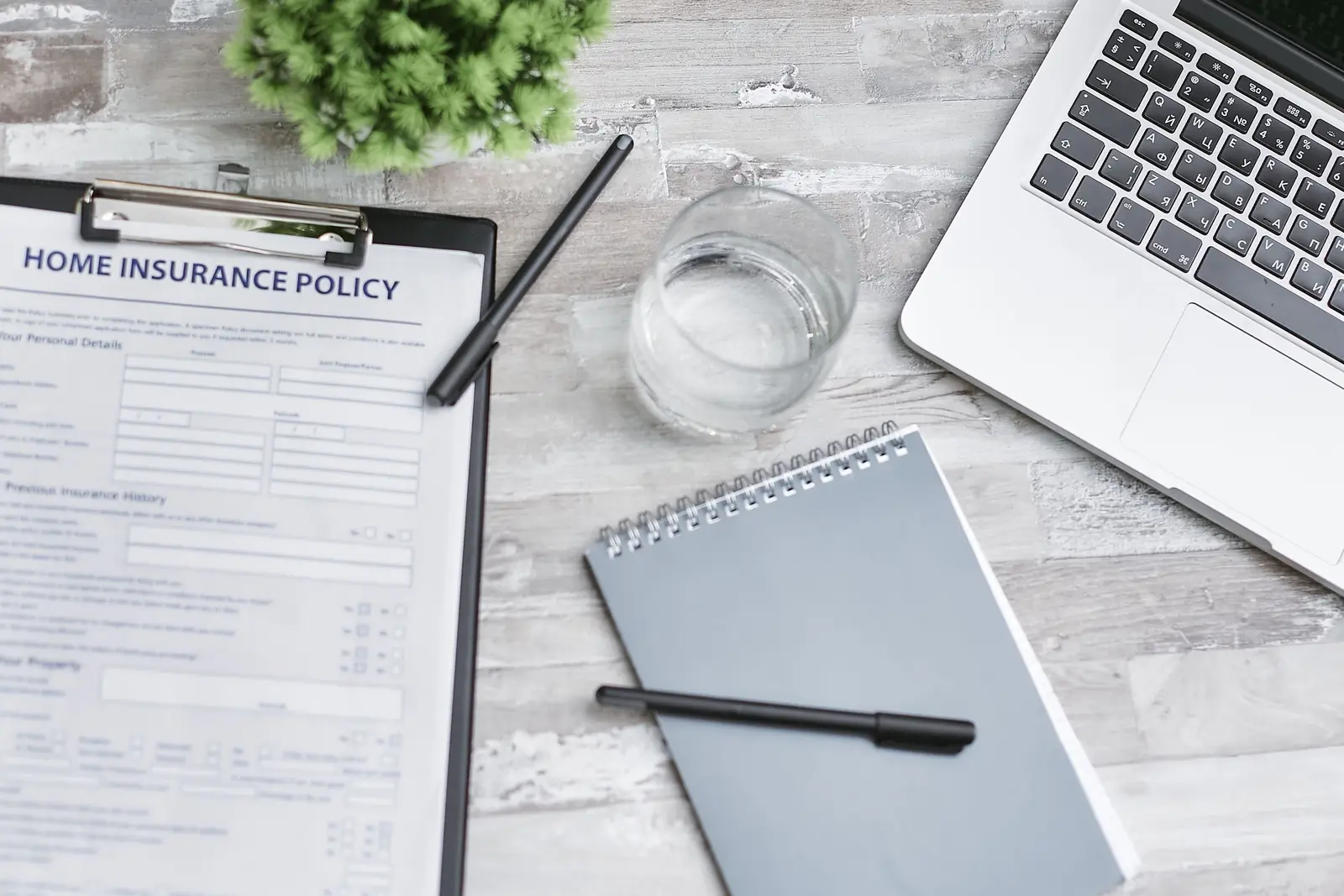 A home insurance policy form on a clipboard beside a laptop and notebook on a desk
