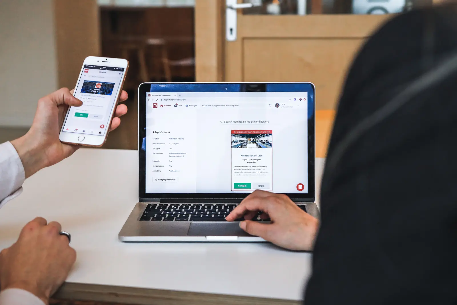 Hands holding a phone with a web page open, next to a laptop showing the same site